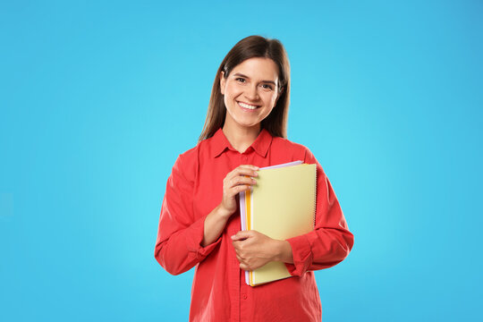 Happy teacher with notebooks on light blue background
