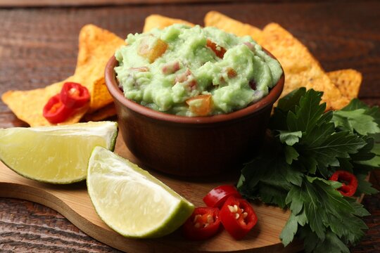 Delicious avocado dip with vegetables in bowl, tortilla chips and products on wooden table, closeup