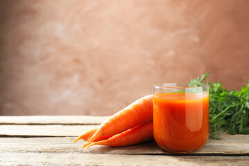 Obraz na płótnie Canvas Fresh carrot juice in glass and ripe vegetables on wooden table, space for text