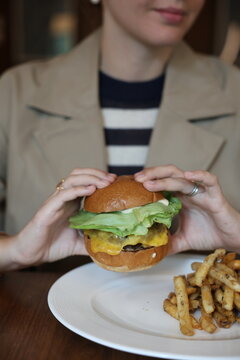 Woman Holding Burger with Fries in Background