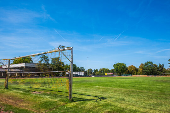 Empty soccer field with goal post in a public sports stadium on a sunny summer day, outdoor green grass pitch with blue sky and trees background