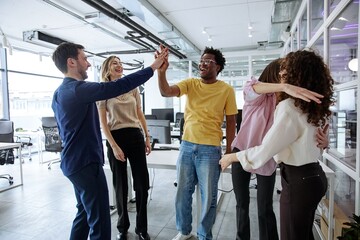 Fototapeta premium Diverse business team giving high-five during a collaborative office meeting