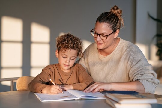 Young student working with tutor on workbook at table with warm sunlight