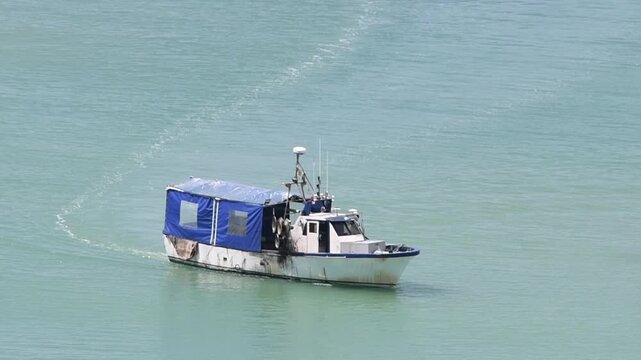 Old commercial fishing vessel with its owner and captain on board moves through a calm sea, leaving a visible trail behind Wake. The crisis of private fisheries in poor countries, seafood production