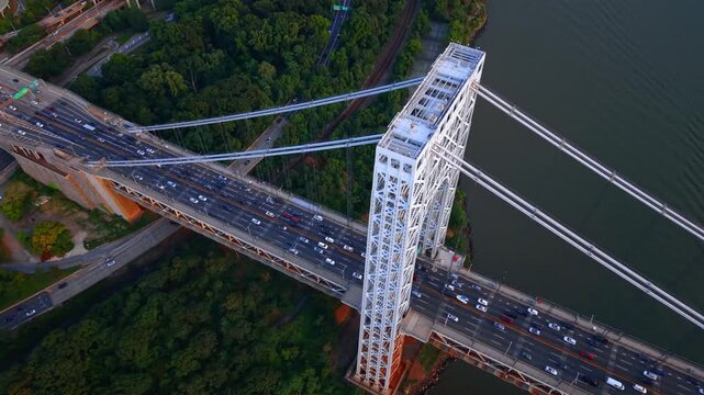Lots of cars move fast by the George Washington Bridge in New York City. Distancing from the river waterfront with lush greenery on.