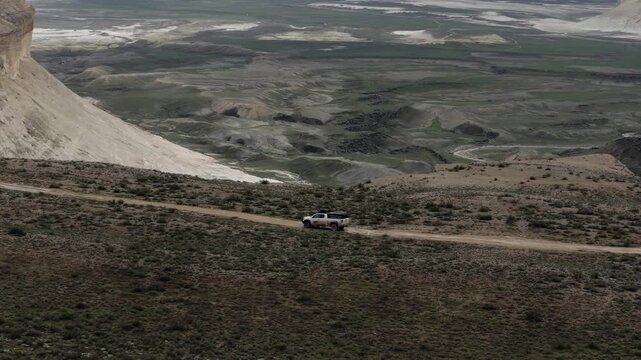 Aerial view of a white off-road vehicle driving on a dirt road through the dramatic limestone landscape of the Bozjyra canyon in Aktau, Mangystau Region, Kazakhstan.