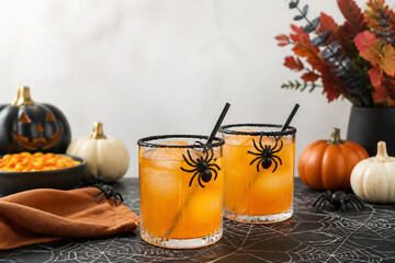 Fototapeta premium Halloween-themed drinks with spider garnishes are displayed on a dark surface near pumpkins and autumn foliage.