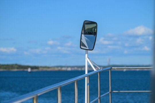 Ferry side mirror and metal railing overlooking Swedish coastal waters.