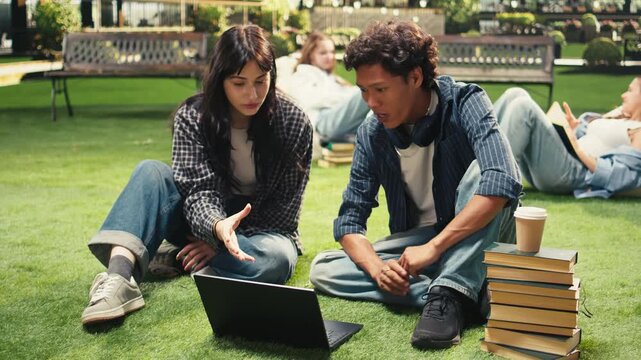 Cheerful students sit on the grass and share ideas in a project discussion, learning together as classmates and friends on a modern campus.