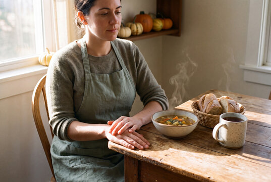 Woman in sage apron sitting with vegetable soup bread and tea