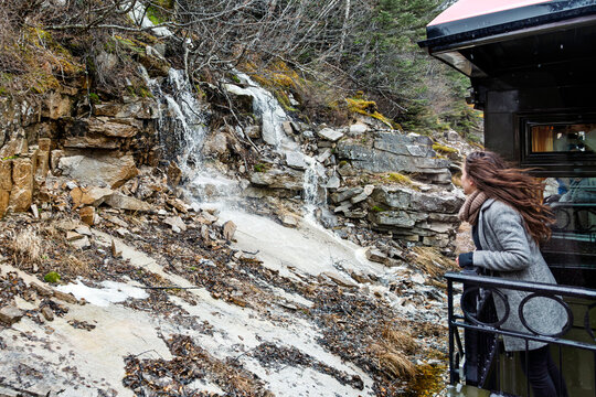 The historic 1898 vintage narrow-gauge train travels the White Pass and Yukon Route Railway as a woman on the observation deck enjoys the rugged frozen landscape in Skagway, Alaska.