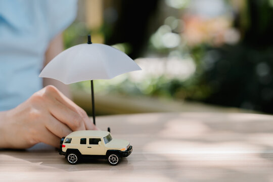 Hand protecting toy car with umbrella, cheerful concept of vehicle insurance, safety coverage and reliable protection for driver