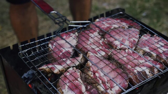 Grilled meat on a barbecue grill with visible flames and smoke, showcasing a close-up view of juicy steaks cooking outdoors in a natural setting