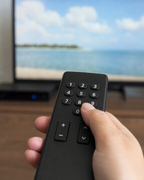 Close-up of hand pressing button on television remote control with blurred screen