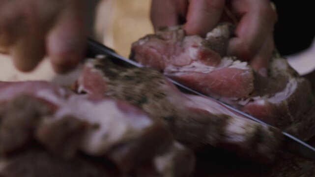 Close-up of hands slicing through a piece of meat with a sharp knife on a wooden cutting board, showcasing the texture and details of the meat during preparation