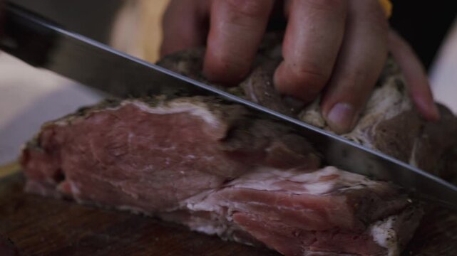 Close-up of seasoned meat being sliced on a wooden cutting board, with hands holding the knife and meat, showcasing the texture and color of the cut