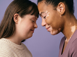 Fototapeta premium Two diverse women touching foreheads against purple background