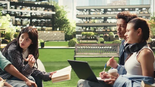 Woman student discusses project notes with classmates near an open laptop on a university campus bench, supporting peer tutoring, collaborative group study, academic teamwork and project work.