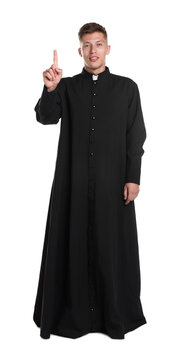 Young priest in cassock pointing upwards on white background