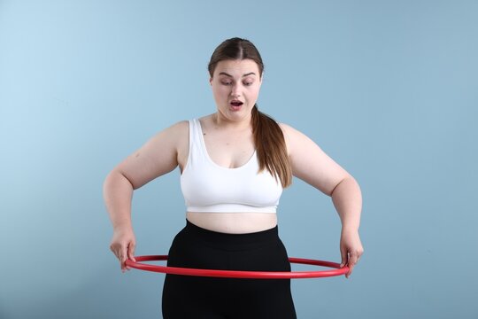 Emotional overweight woman with hula hoop on light blue background