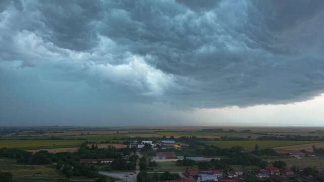 Dramatic supercell thunderstorm forming over rural farmland, with massive dark shelf clouds, heavy rainfall and turbulent storm structure creating an ominous severe weather landscape.