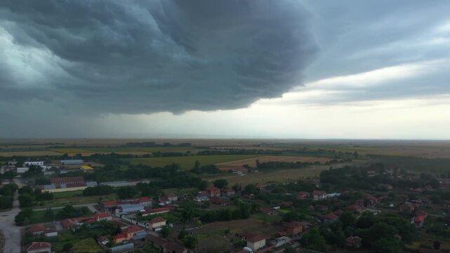 Dramatic supercell thunderstorm forming over rural farmland, with massive dark shelf clouds, heavy rainfall and turbulent storm structure creating an ominous severe weather landscape.