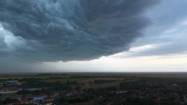 Dramatic supercell thunderstorm forming over rural farmland, with massive dark shelf clouds, heavy rainfall and turbulent storm structure creating an ominous severe weather landscape.