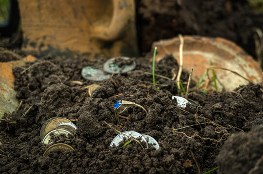Found treasure concept. Coins and a ring with a blue stone on a background of fragments from a clay pot, a mixture of soil and old metal artifacts are also visible