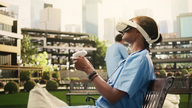 The medical student uses VR controllers and a headset on a wooden bench, practicing immersive healthcare learning outdoors on a sunny campus lawn in blue scrubs for medical training.