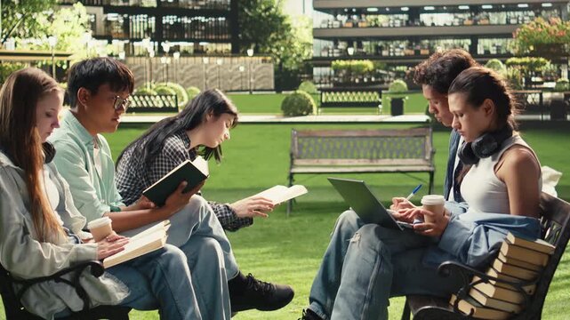 Students read project notes together on a wooden bench at a university campus, supporting peer tutoring, teamwork and collaborative academic learning during a focused group study session.