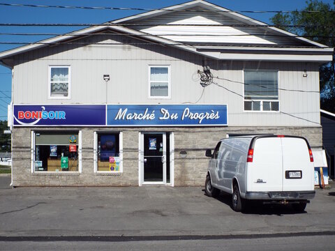 Gatineau, Quebec, Canada &ndash; June 21, 2026: A white delivery van parked in front of "March&eacute; Du Progr&egrave;s and Bonisoir" store building under a clear blue sky at 176 Rue Saint-Antoine