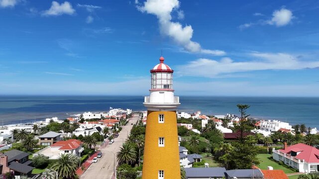 Aerial drone view circling the iconic Punta del Este Lighthouse, revealing the Atlantic Ocean, coastal neighbourhood and blue skies in Punta del Este, Uruguay.