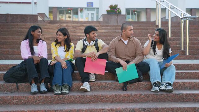 Group of indian students sitting on stairs talking and smiling