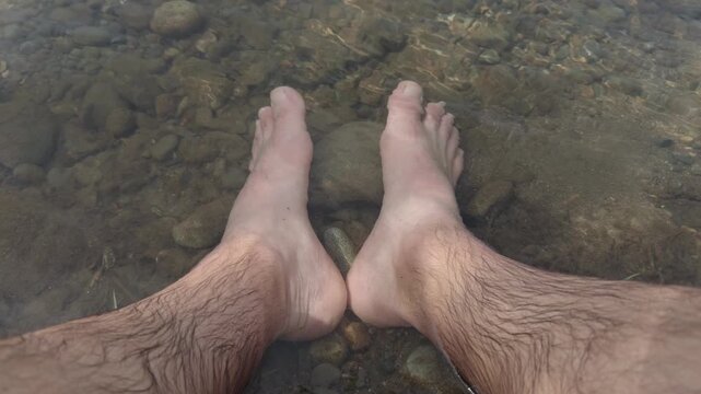 Bare male feet soaking in clear shallow creek water