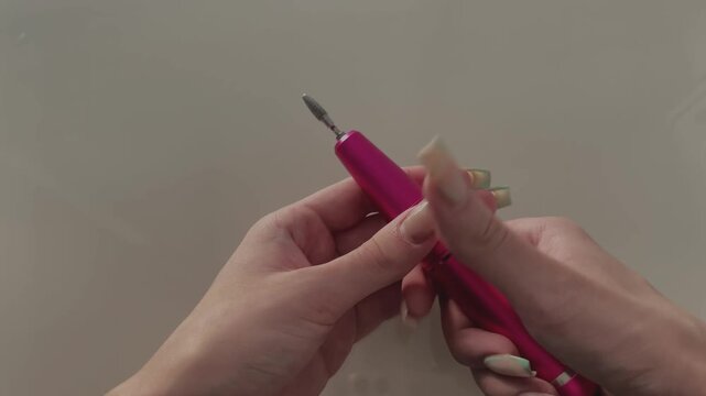 Professional manicurist inserting a metal bit into an electric nail drill for salon procedures