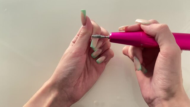 Female hands using a professional electric nail file to remove gel polish on a white background