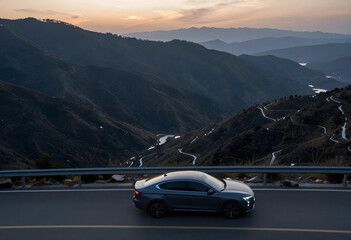 Obraz premium Dark gray sedan driving on a winding mountain road at sunset with a scenic valley view