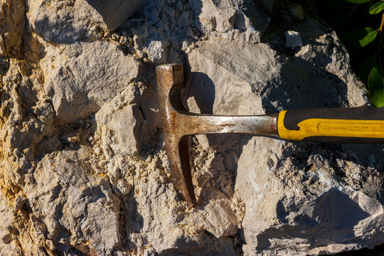 Close-up of a steel geological hammer resting on raw limestone rock at a quarry, used for expert fossil hunting and exploring mineral samples during outdoor fieldwork expeditions