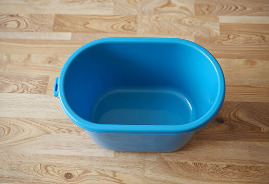 Empty blue plastic basin on a light wooden floor, household cleaning and organization concept, top down view