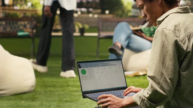 The student analyzes solar panel data for sustainable energy on a laptop, studying photovoltaics and checking a clean energy dashboard on campus for renewable energy research and data analysis.