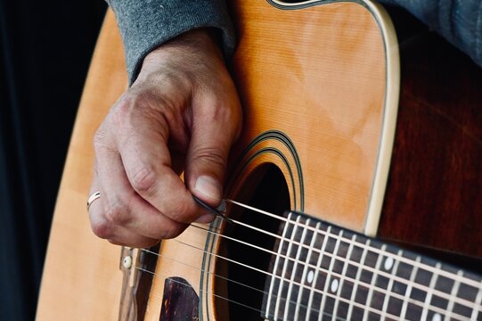 Selective focus macro view capturing fingers picking steel wires near soundhole during live session.