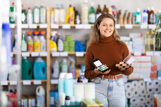 Uncertain young girl holding cosmetic products trying to make choice while shopping