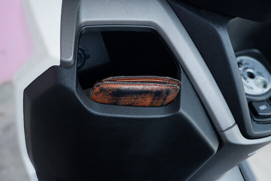 leather wallet accidentally left in the open front compartment of a scooter dashboard, illustrating the risk of theft and carelessness. Ideal for crime prevention campaigns