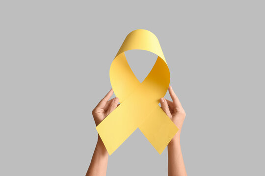 Hands holding a yellow awareness ribbon, a symbol of support for various causes, against a gray background