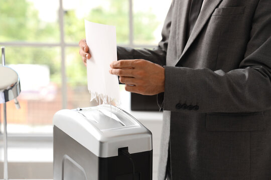 Businessman shredding confidential documents for data protection and privacy in an office setting, the action represents security measures against identity theft and fraud