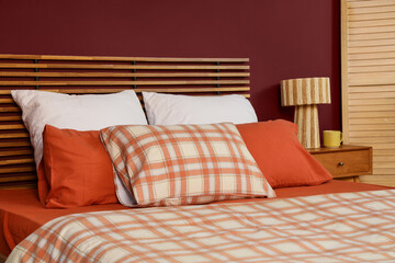 Obraz premium Cozy bedroom interior with a wooden slatted headboard, plaid bedding, and a textured lamp on a nightstand