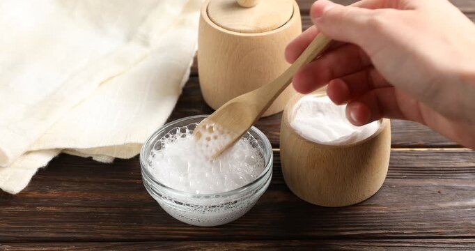 Woman pouring baking soda into bowl with water at wooden table, closeup