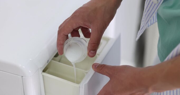 Man pouring liquid laundry detergent into washing machine detergent compartment, closeup