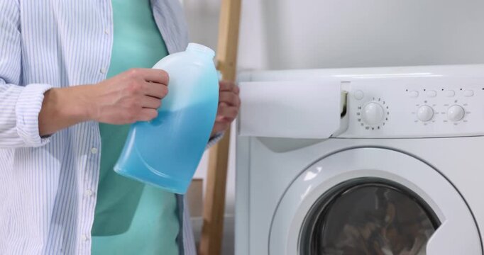 Man pouring liquid laundry detergent from bottle into cap near washing machine, closeup