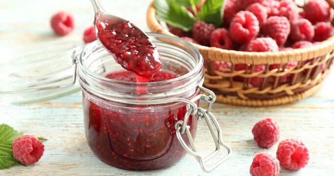 Woman taking delicious raspberry jam with spoon from glass jar at color wooden table, closeup